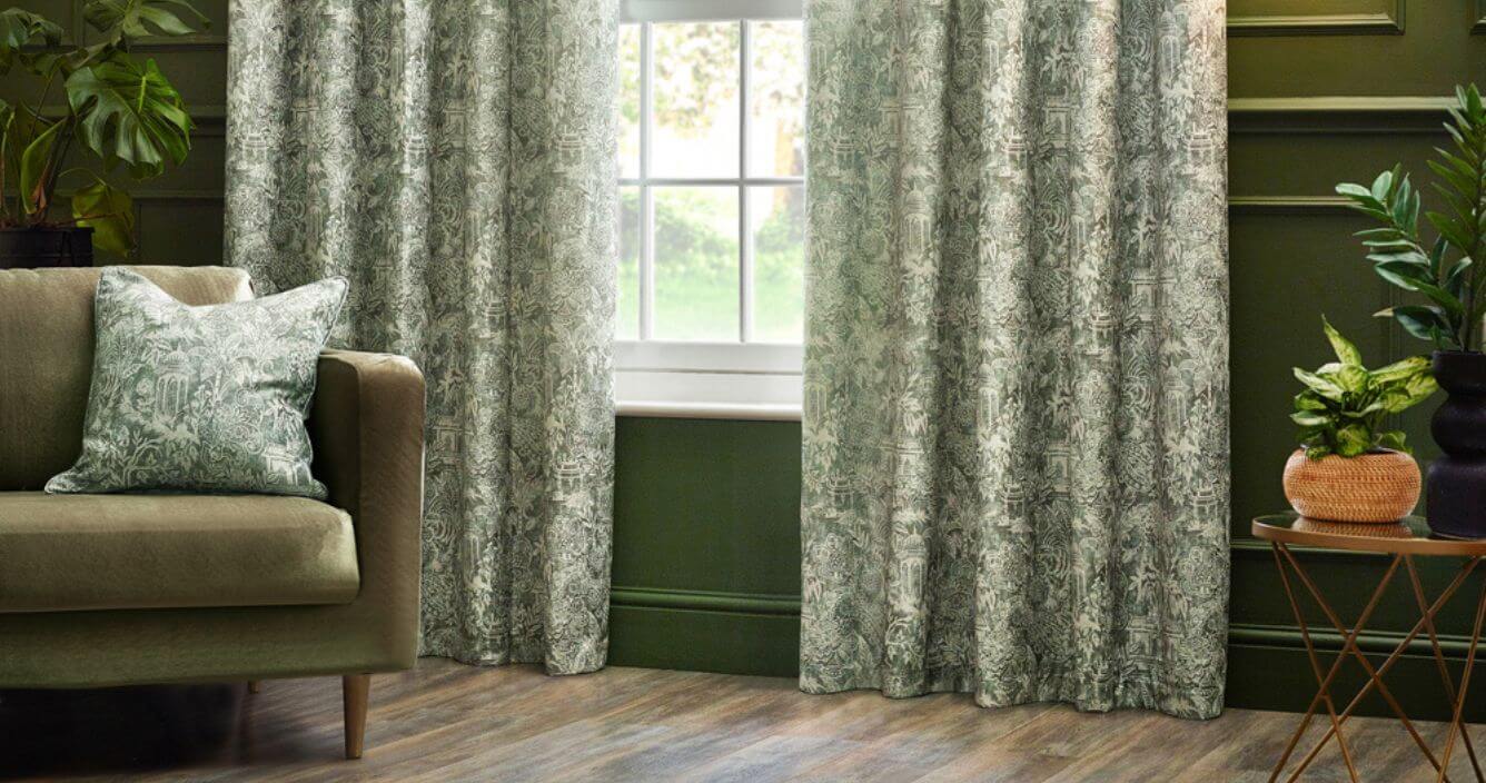 A pair of sage green curtains with a contemporary design of Bengal tigers and jungle foliage, hung in front of an olive green wall in a decorated living room. 