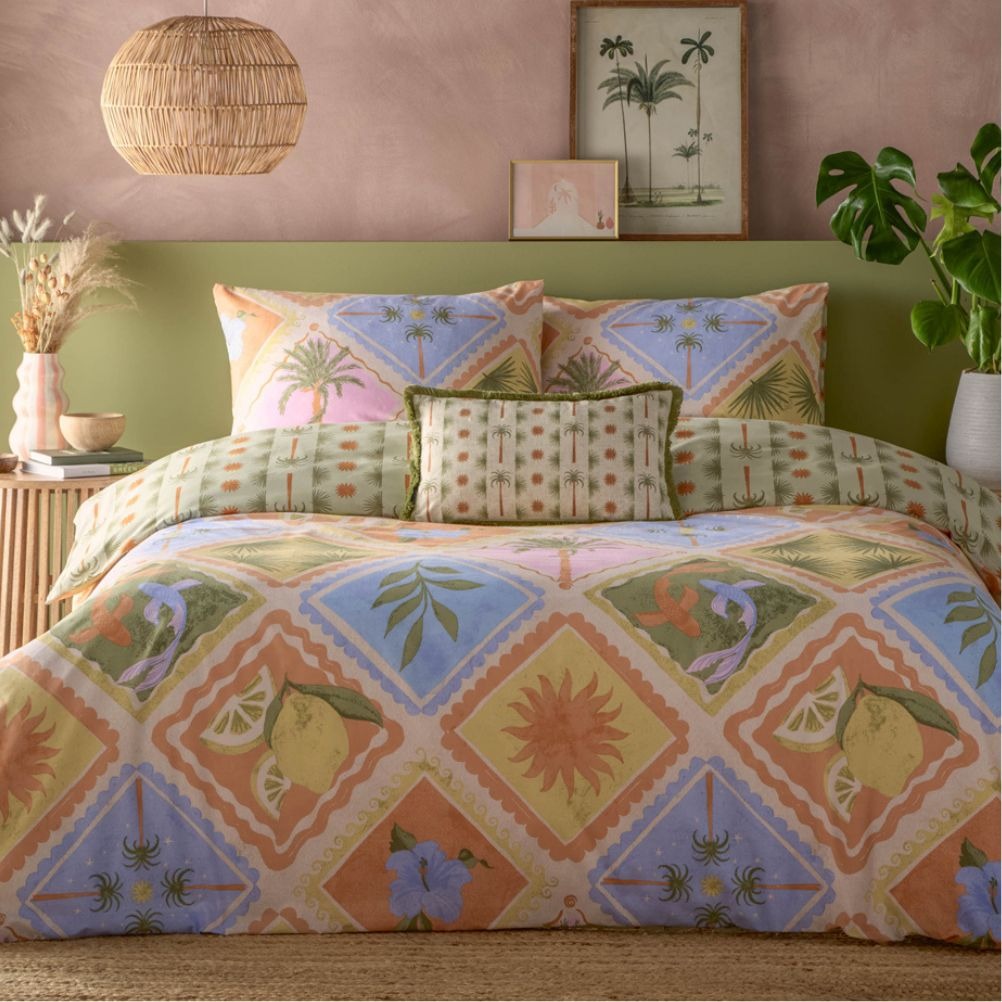 Colourful tropical-themed bedding set with lemons in the pattern, palm pattern cushions and a green headboard. 