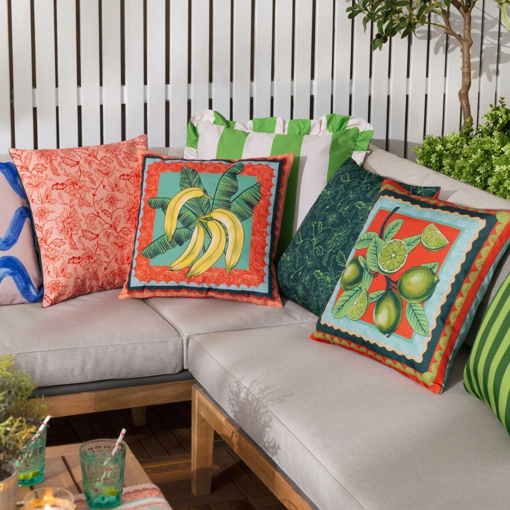 Colourful decorative outdoor cushions with banana and lime designs on a light gray sofa in the garden. 