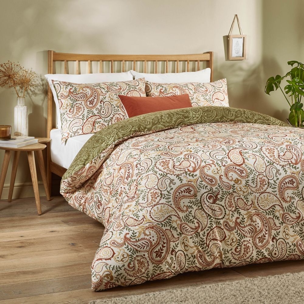 Bed with paisley patterned print and orange cushion