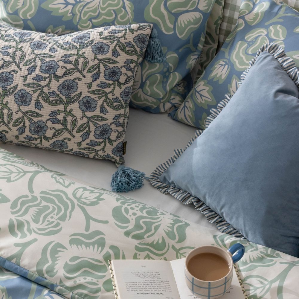 Floral cushions, next to blue velvet cushion with frilled edge on a floral duvet cover