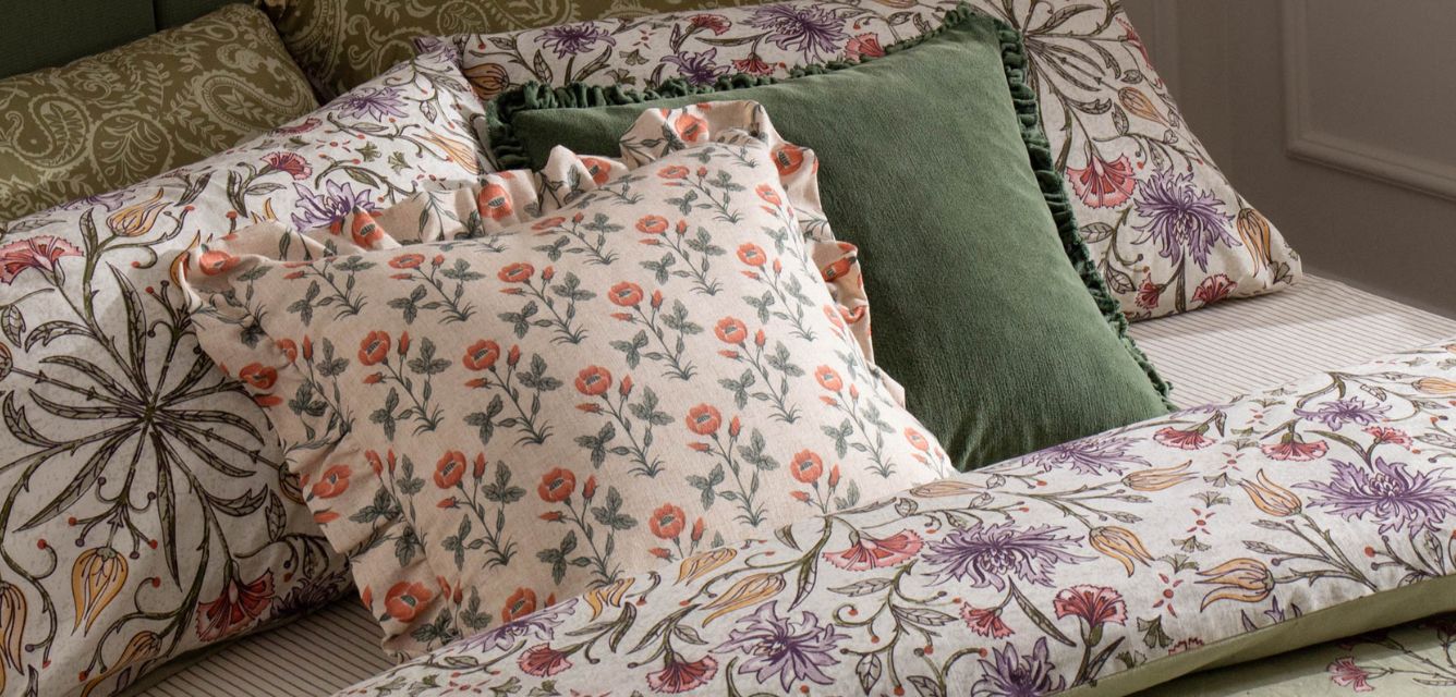 Pattern clashing cushions with florals and paisleys, with a green velvet cushion on a floral duvet cover