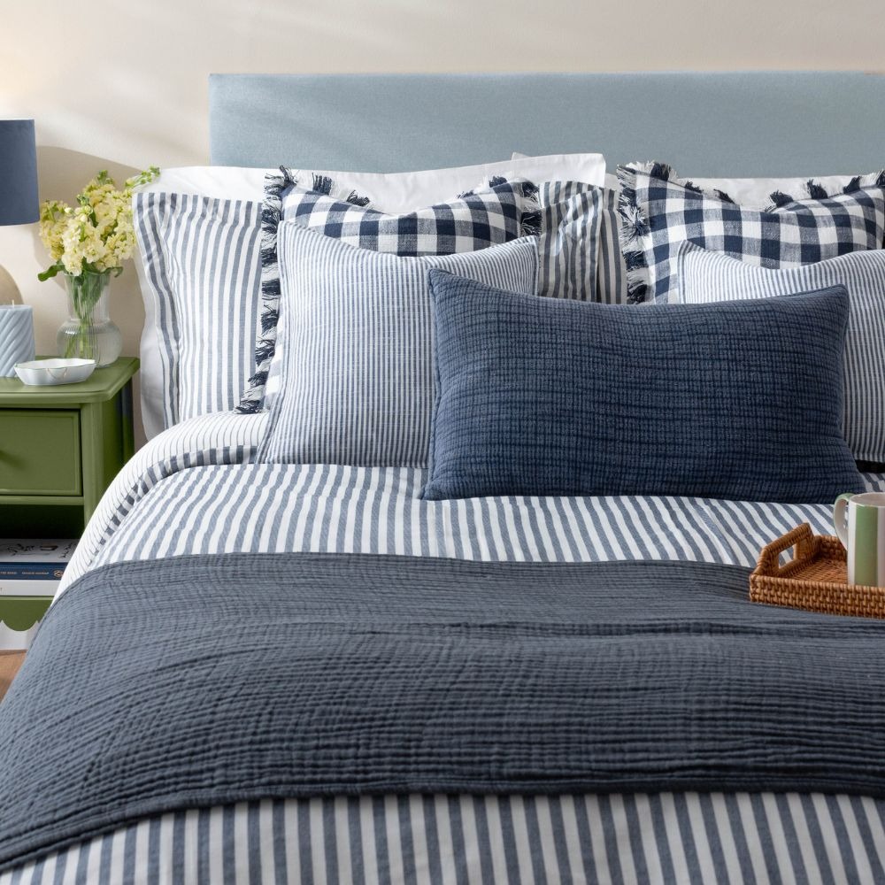 Blue colour drenched bedroom with blue striped bedding, blue cushions and a blue throw blanket