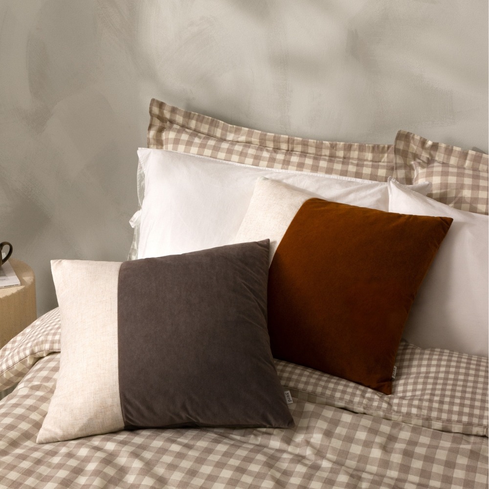 beige check bed with brown and red velvet cushions with a cream wide stripe on the left hand side