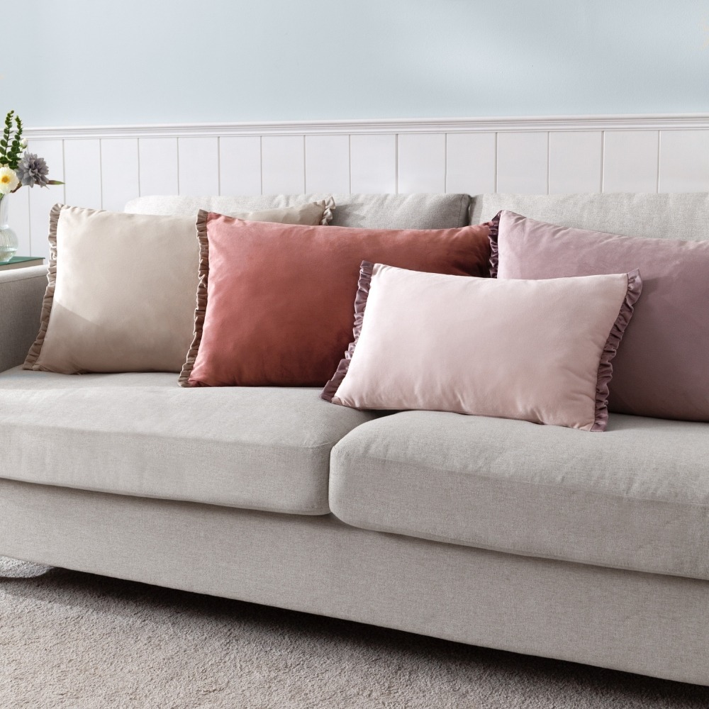 light grey sofa, light blue wall, with pink, red, purple and beige frilly velvet cushions