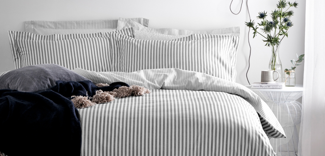 Grey striped bedding with a dark grey throw against a white wall