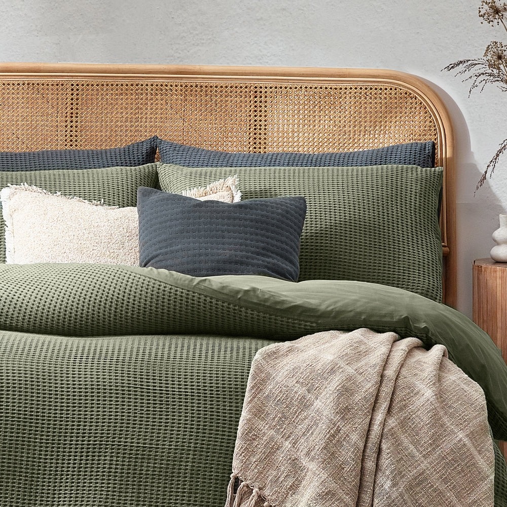 green waffle textured bedding with grey cushions, a white cushion and a beige throw.