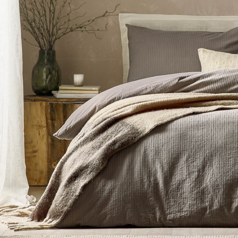 grey bedding with a cream cushion and neutral beige throw.
