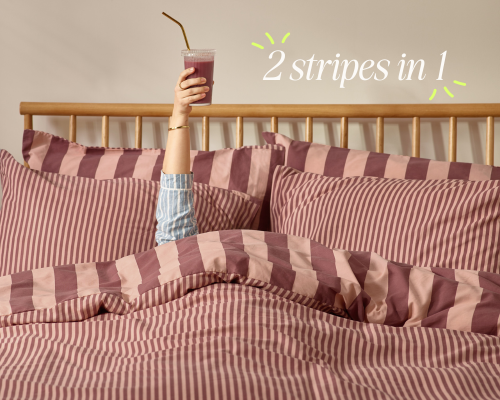 A reversible stripe duvet cover in pink and darker pink, with an arm coming out of the bed holding a raspberry smoothie