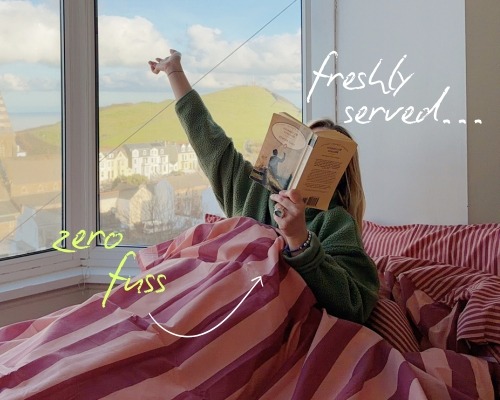 A pink wide striped bedding with a girl in the covers reading a book showing the striped duvet does not require ironing