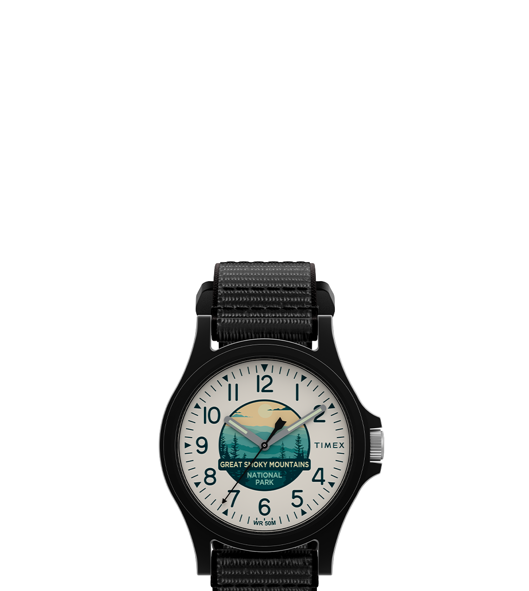 Front-facing product image of the Timex x Great Smoky Mountains National Park watch. The watch features a black case and strap, white dial with black numerals, and an illustrated national park scene with a bear, forest, and sunrise graphic.