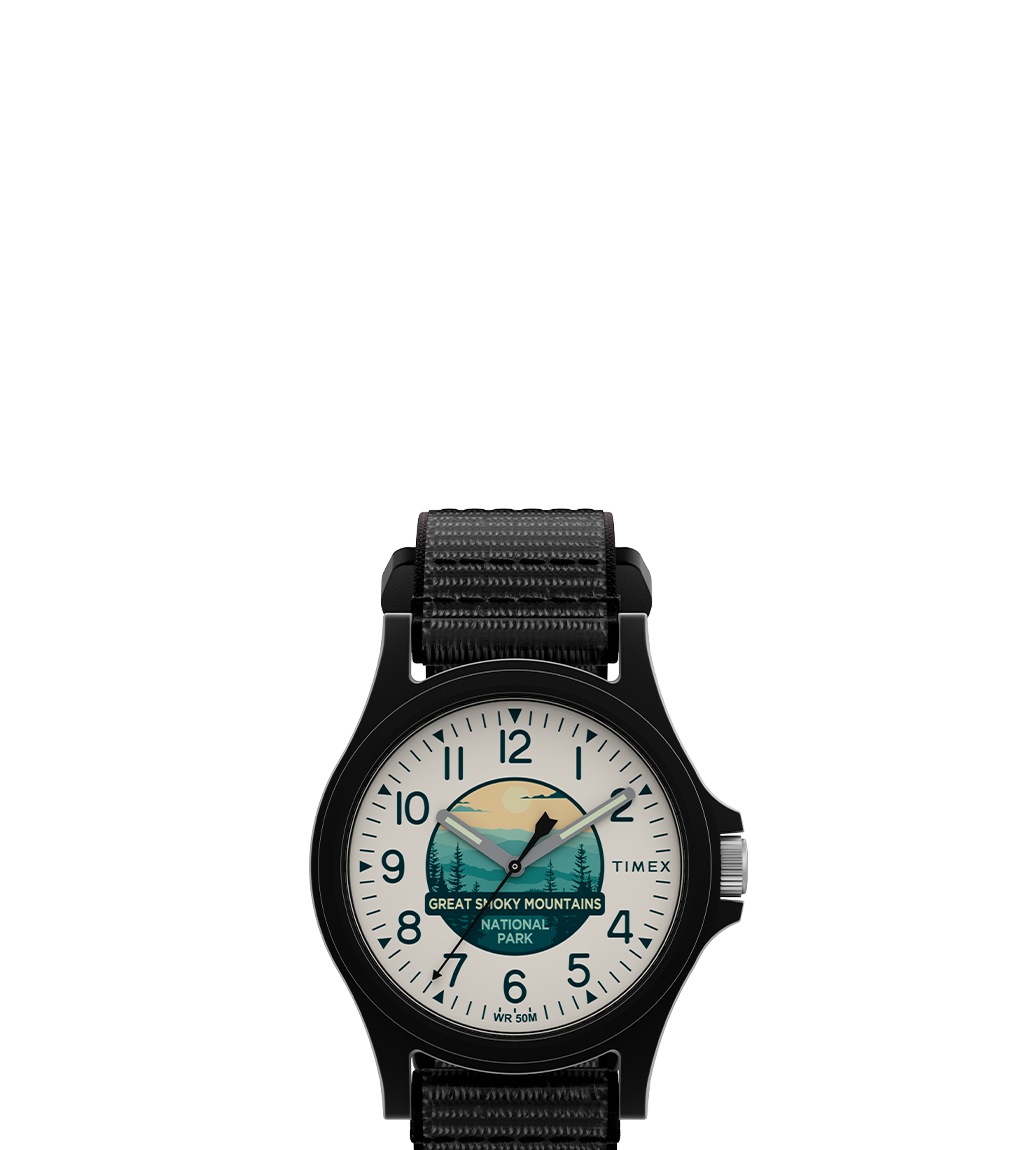 Front-facing product image of the Timex x Great Smoky Mountains National Park watch. The watch features a black case and strap, white dial with black numerals, and an illustrated national park scene with a bear, forest, and sunrise graphic.