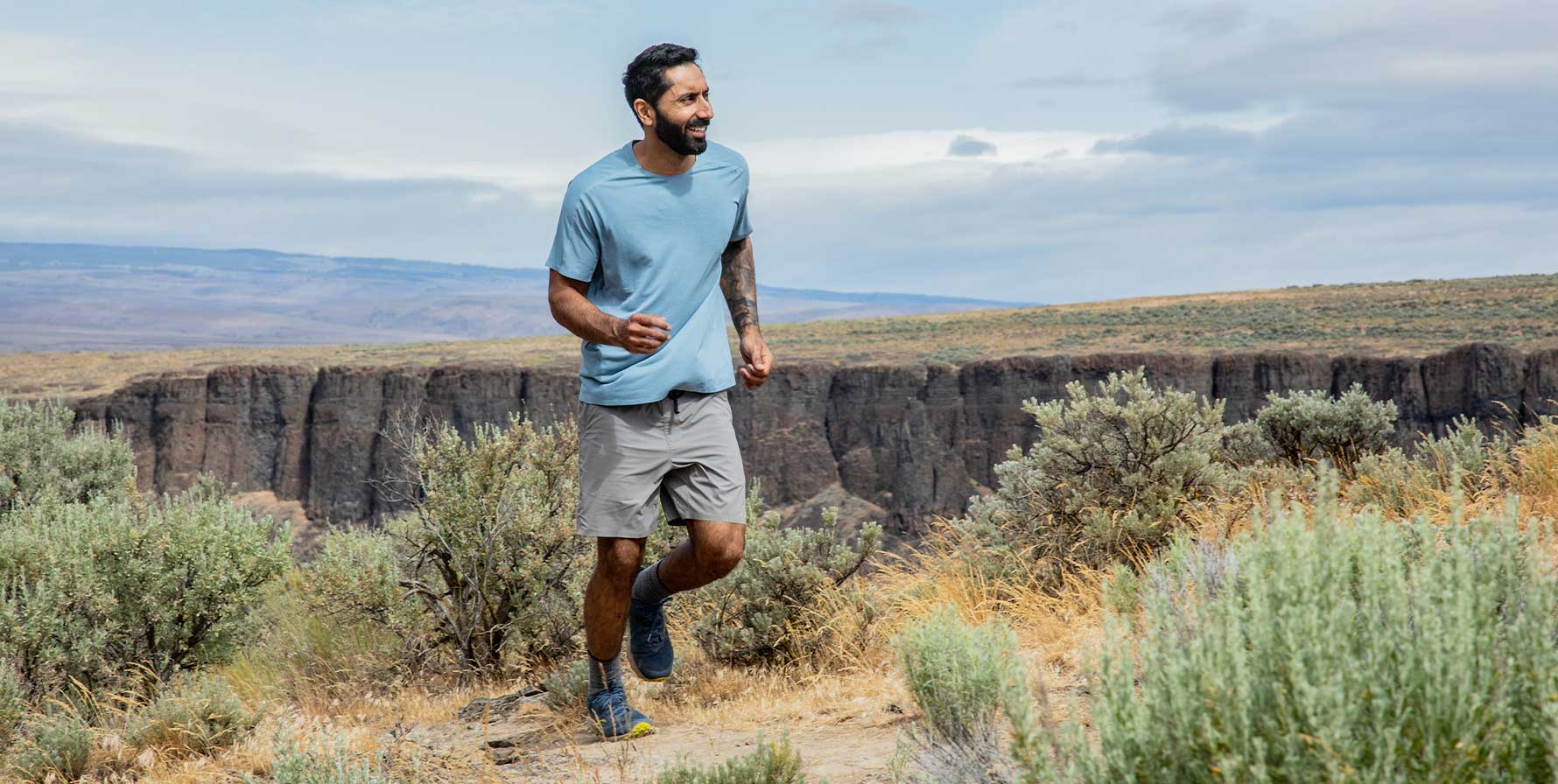 Man wearing the Moonstone TarnGood Short and the Big Sky Blue SolarSwift Tech-T. Trail Running through the high desert environment with a vast blue sky in the background.