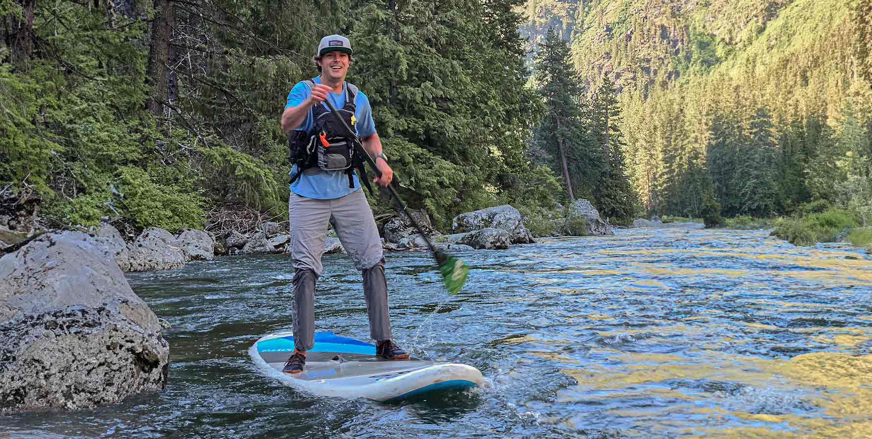 Man wearing the Moonstone TarnGood pant while stand up paddle boarding on a forested mountain creek. Also wearing the Big Sky Blue SolarSwift Tech-T.