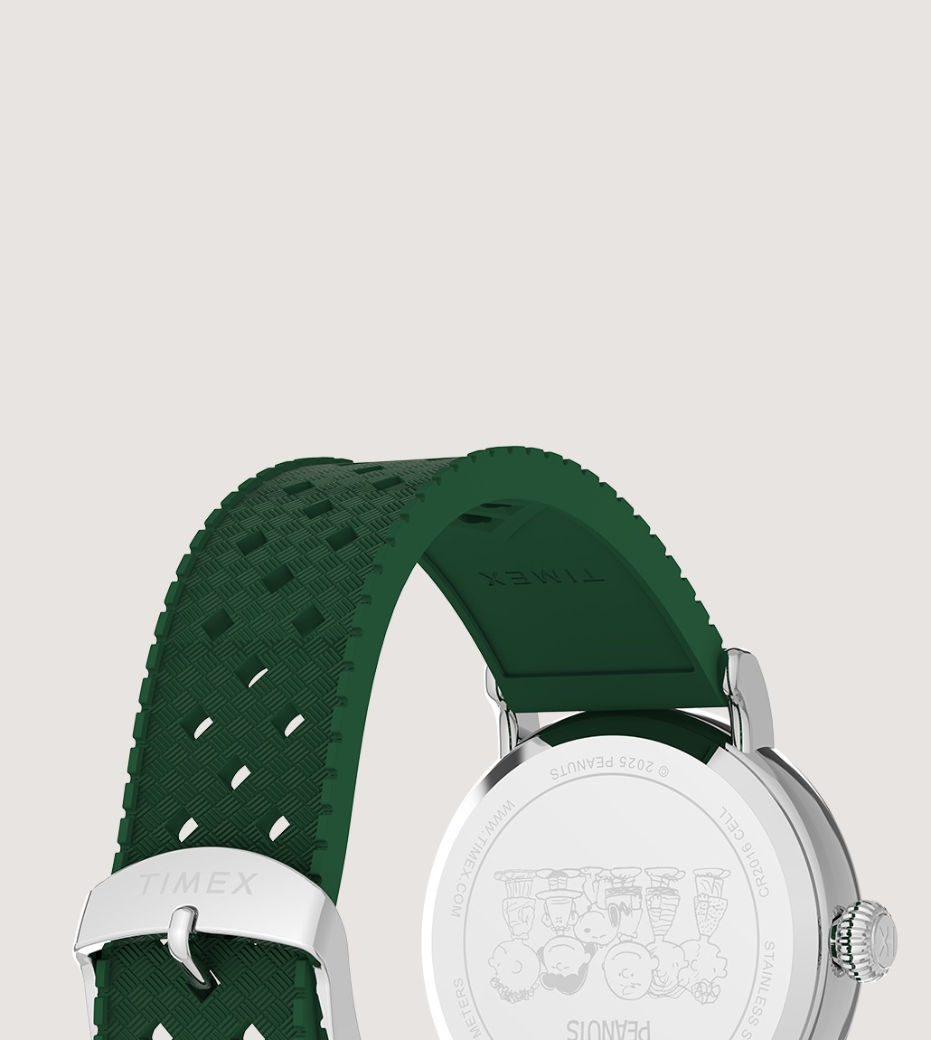 The stainless steel case back features an engraved illustration of Peanuts characters. The watch has a green strap with a textured, perforated design and a Timex-branded silver buckle.