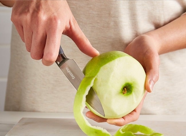 A person slicing a green apple with the GreenPan Titanium Cutlery. 