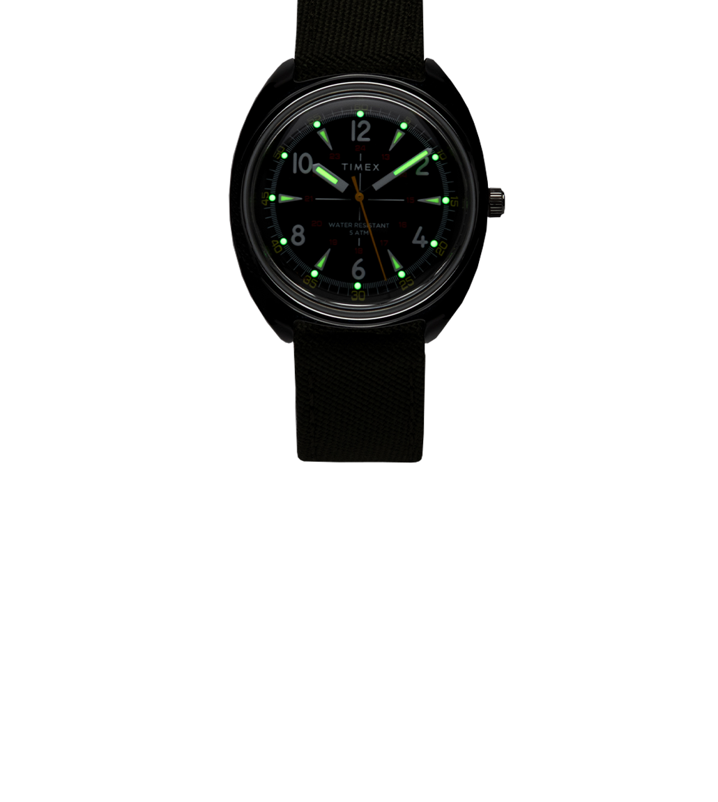 Timex x Bespoke Post watch in a dark setting with glowing green luminous hour markers and hands, highlighting its nighttime visibility.