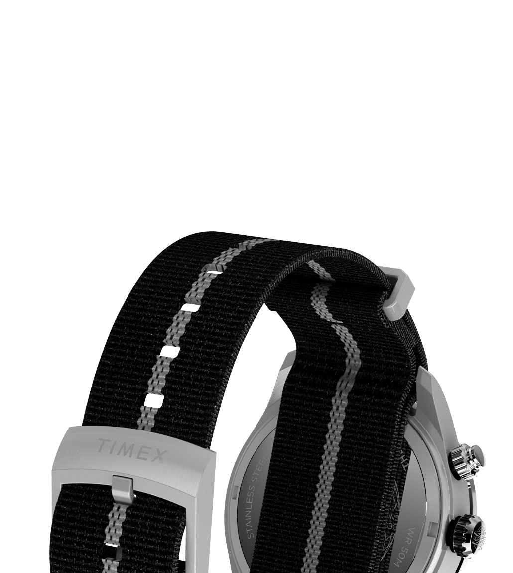 Detail image of the Timex Waterbury Heritage Chronograph’s black fabric strap with a white stripe, silver buckle engraved with “TIMEX”, and a partial view of the stainless steel case back and lugs.