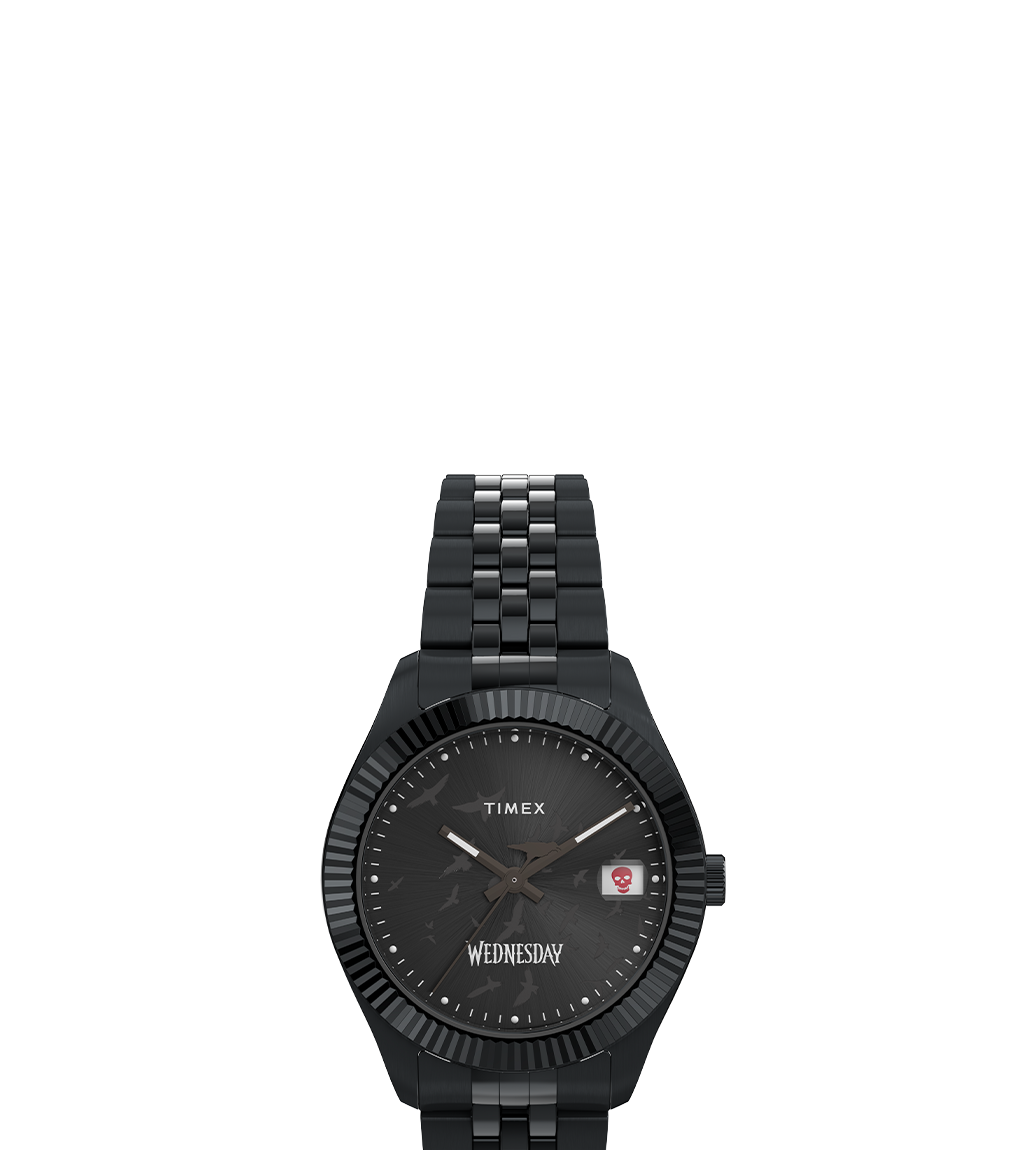 Front-facing view of the Timex x Wednesday Legacy watch, showcasing a black case, black dial with raven details, a red skull icon in the date window, and the “Wednesday” logo at the 6 o’clock position, paired with a polished black link bracelet.