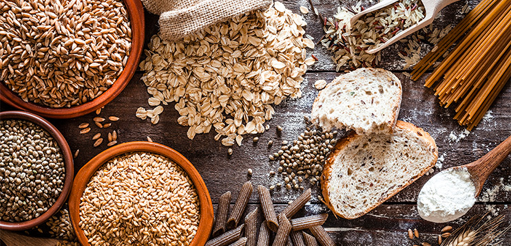 Piles of whole grains and seeds on a table representing food sources of Magnesium.