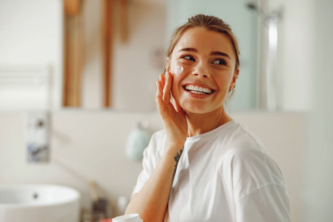 Person applying face cream while standing in a bathroom