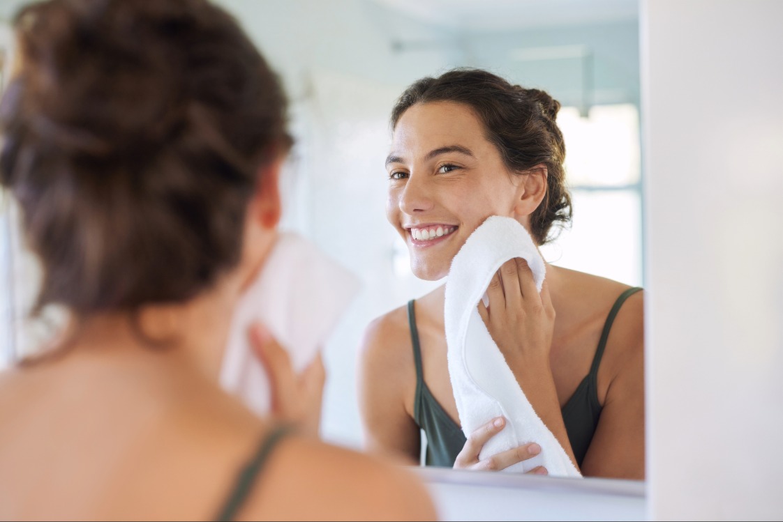 Person dabbing face with a towel while looking in a bathroom mirror