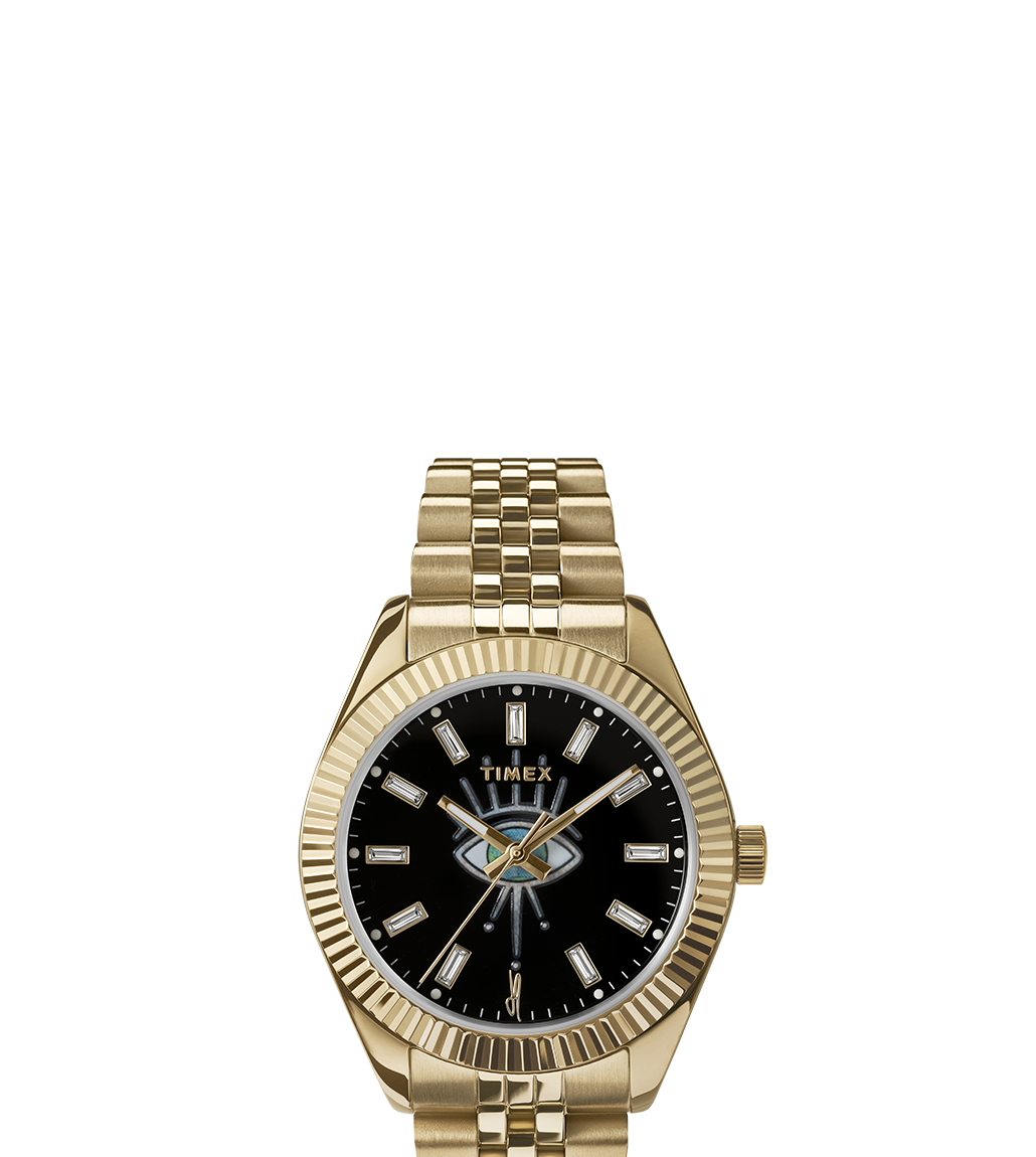 Front view of the Timex x Jacquie Aiche watch with a black dial and gold-tone casing and bracelet. The dial showcases the artistic eye design at the center, crystal hour markers, and gold-tone hands within a ridged bezel.