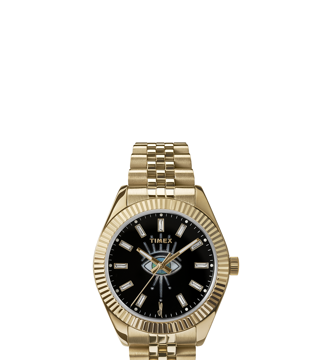 Front view of the Timex x Jacquie Aiche watch with a black dial and gold-tone casing and bracelet. The dial showcases the artistic eye design at the center, crystal hour markers, and gold-tone hands within a ridged bezel.