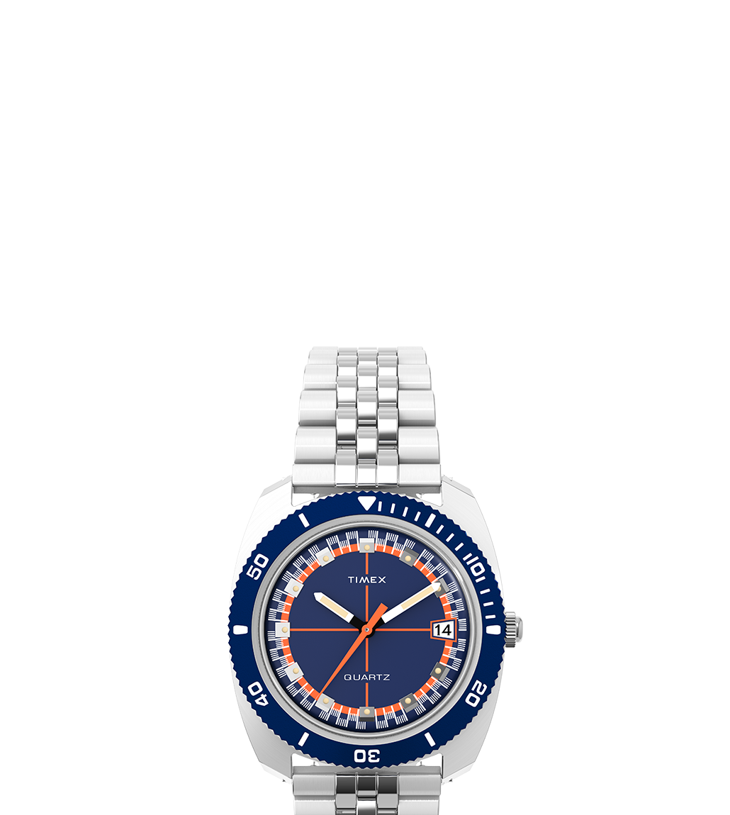 Product shot of the Q Timex® 1971 Velocity on a white background. The full watch is shown vertically, highlighting its polished bracelet, deep navy blue dial, and rotating bezel.