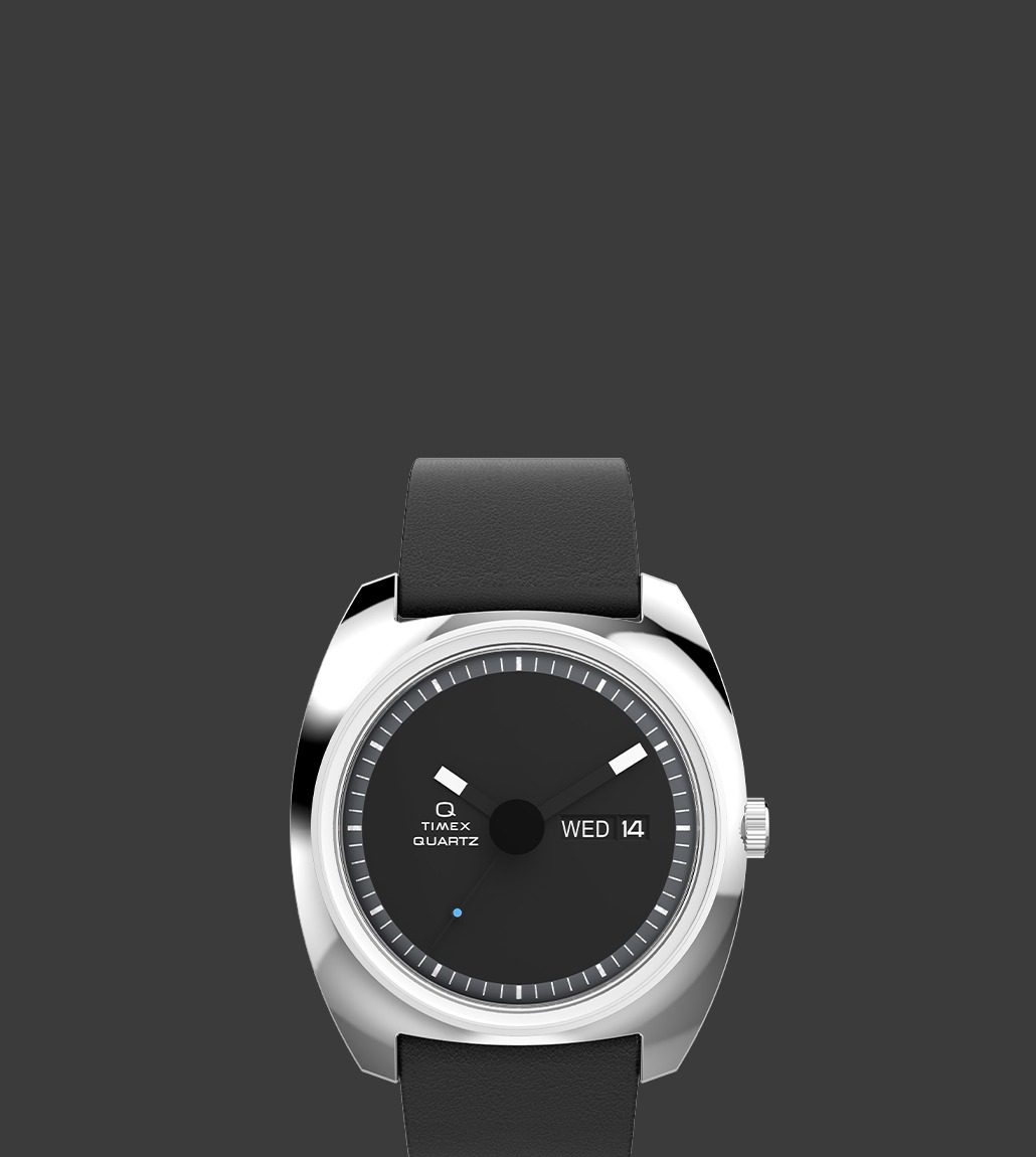 Front view of the Q Timex® 1975 Enigma watch showcasing a minimalist black dial, silver-tone case, bold white hour markers, and day-date display on the right side. The watch has a smooth black leather strap.