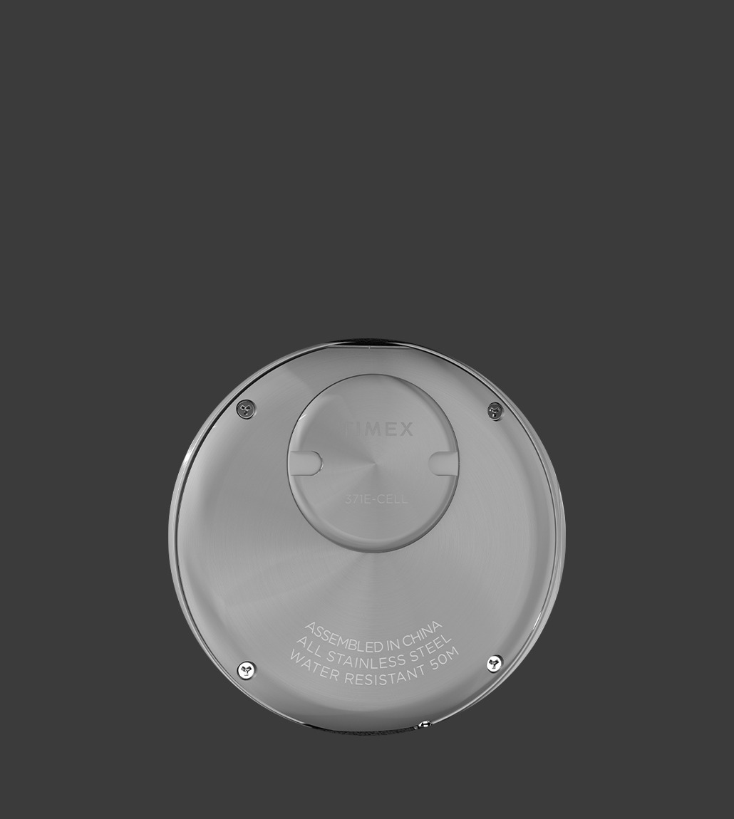 Back view of the Q Timex® 1975 Enigma watch featuring a brushed stainless steel case back engraved with text indicating assembly in China, water resistance of 50 meters, and use of a 371E-cell battery.