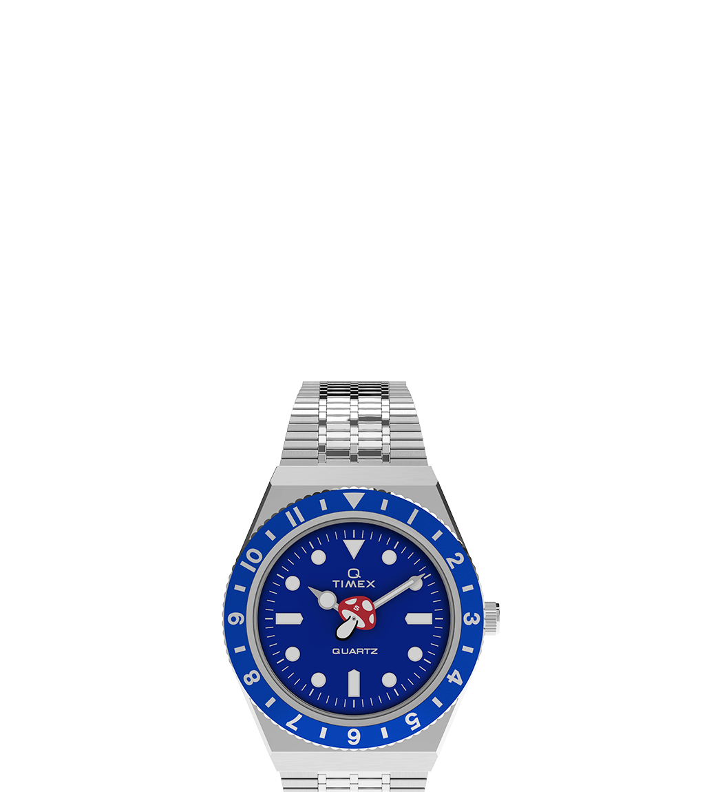 Straight-on view of the Timex x seconde/seconde/ Episode 0 watch with blue dial and bezel, red mushroom hour hand, and a stainless steel bracelet. Branding and dial details are clearly visible.