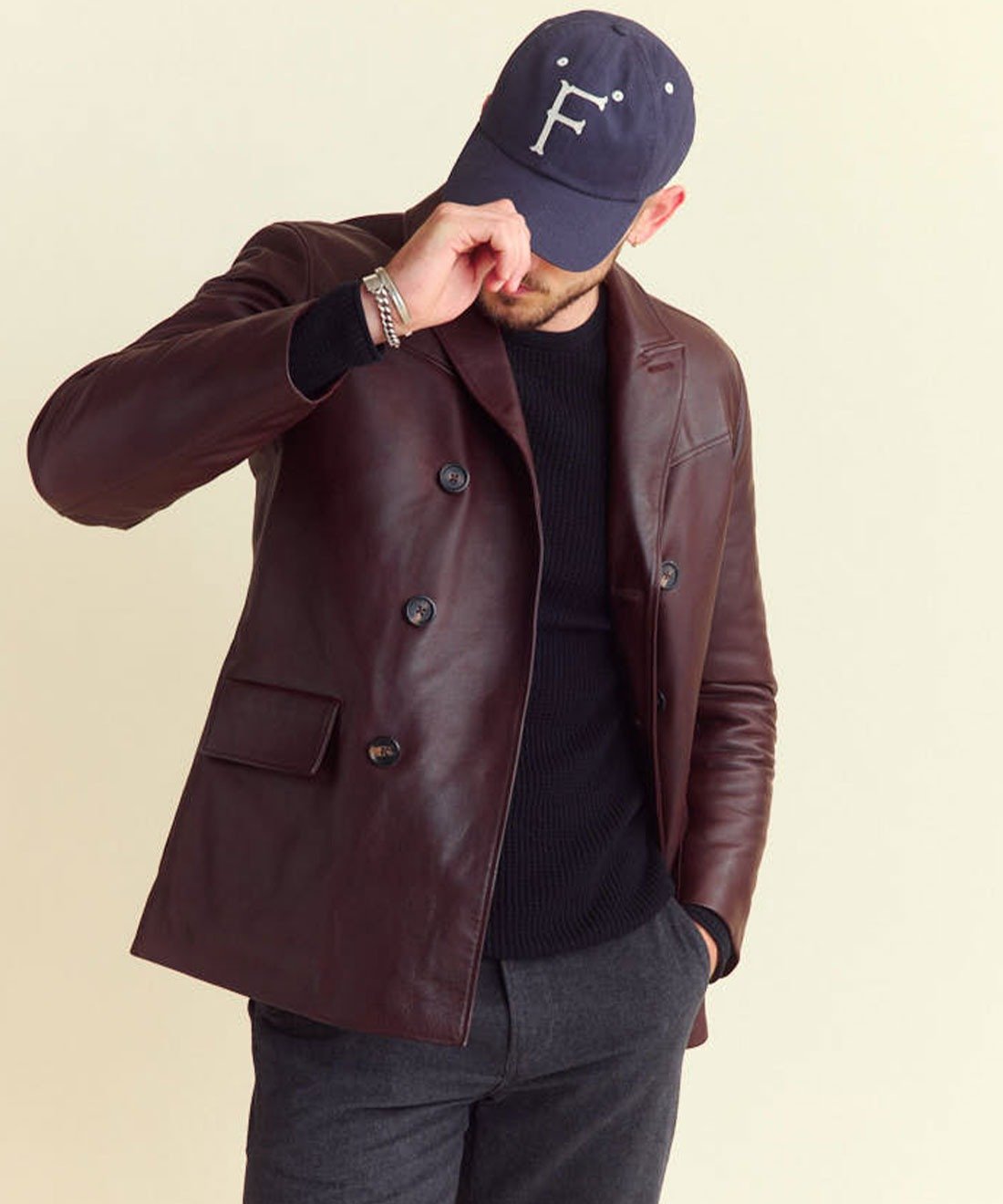 Man wearing brown leather jacket and navy cap with 'F' logo.