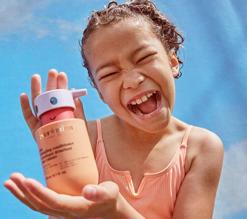 Smiling child holding Evereden shampoo bottle.