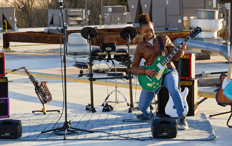 a person playing a green beginner electric guitar in front of a drum set, amplifiers, mic stand, and e flat alto sax