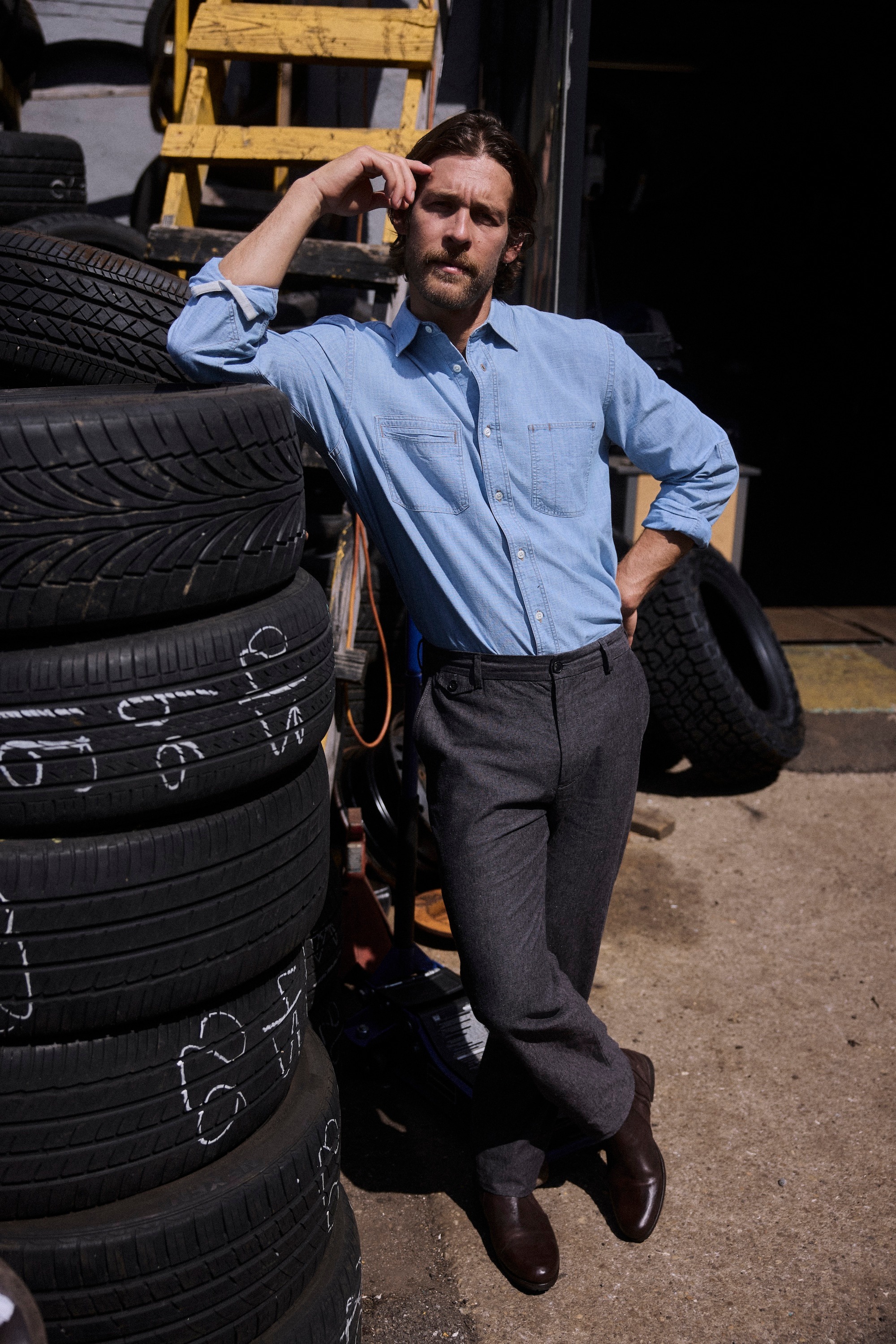 Model wears the Chambray Field Shirt while leaning against tires.
