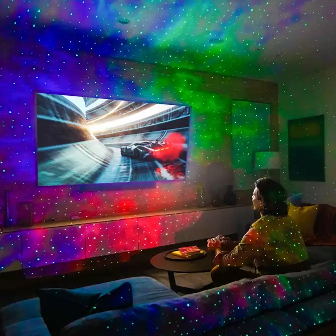 man playing video games with multicolor galaxy lights in living room