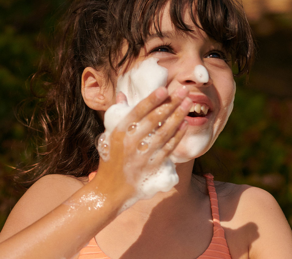 Young boy applying moisturizer to his cheek.
