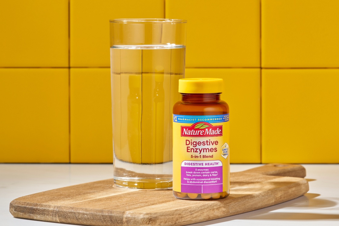 Nature Made Digestive Enzymes 5-in-1 Blend Bottle on a cutting board next to a glass of water.