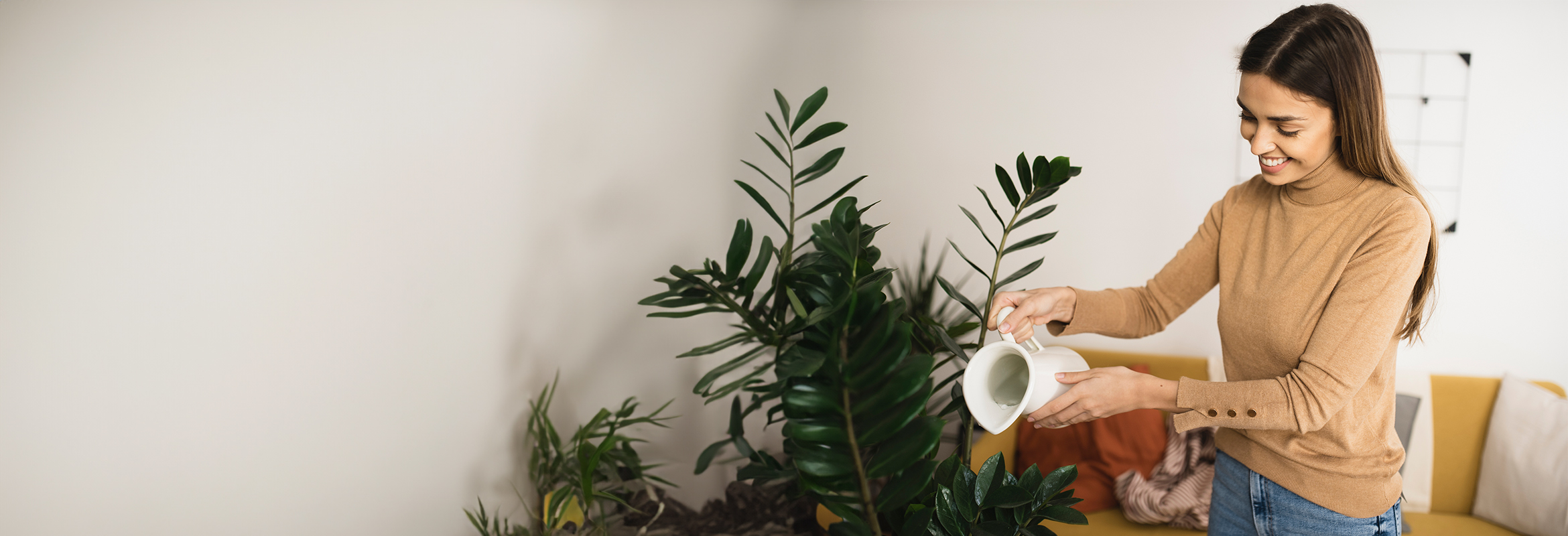 Woman in tan top watering a plant indoors.