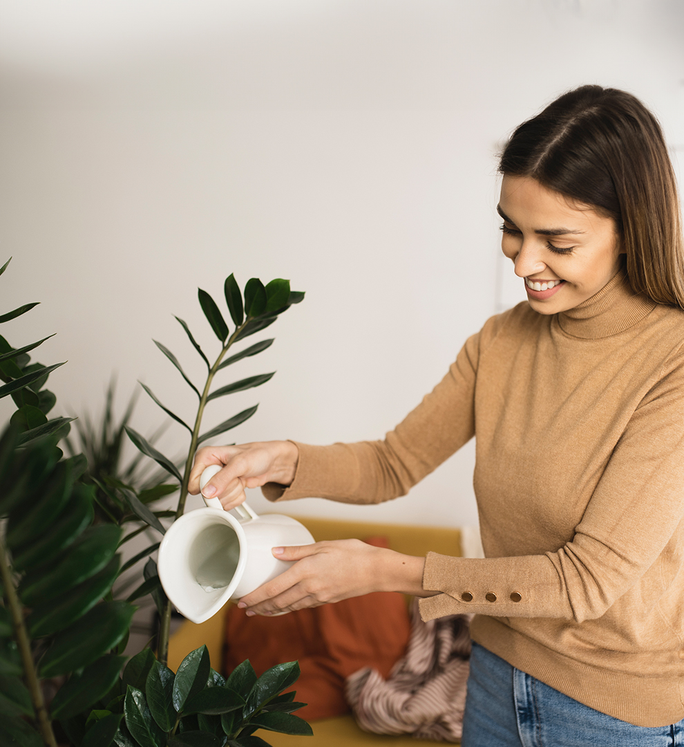 Woman in tan top watering a plant indoors.