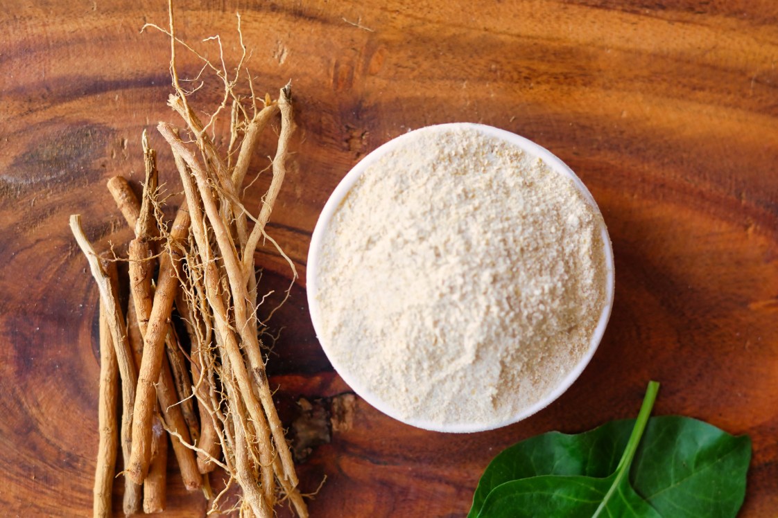 Ashwagandha roots and a bowl of ashwagandha powder on a wooden table.
