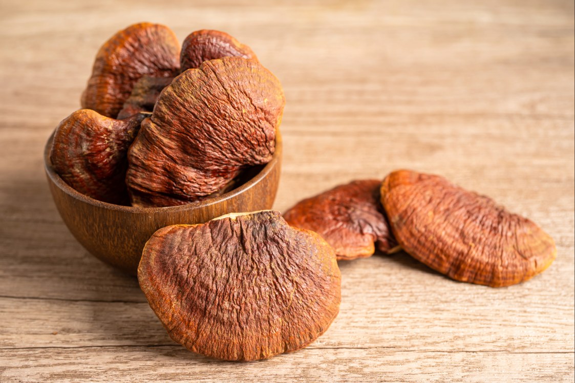 Reishi mushroom caps in a bowl on a wooden surface.
