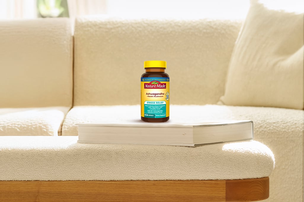 Nature Made Ashwaghanda + Reishi Mushroom Capsules bottle on top of a book in a living room setting.