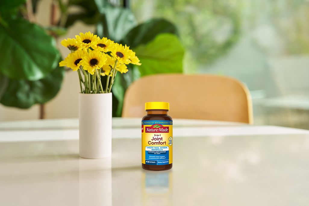 Nature Made 3‑in‑1 Joint Comfort capsules on table with flowers for joint health support.