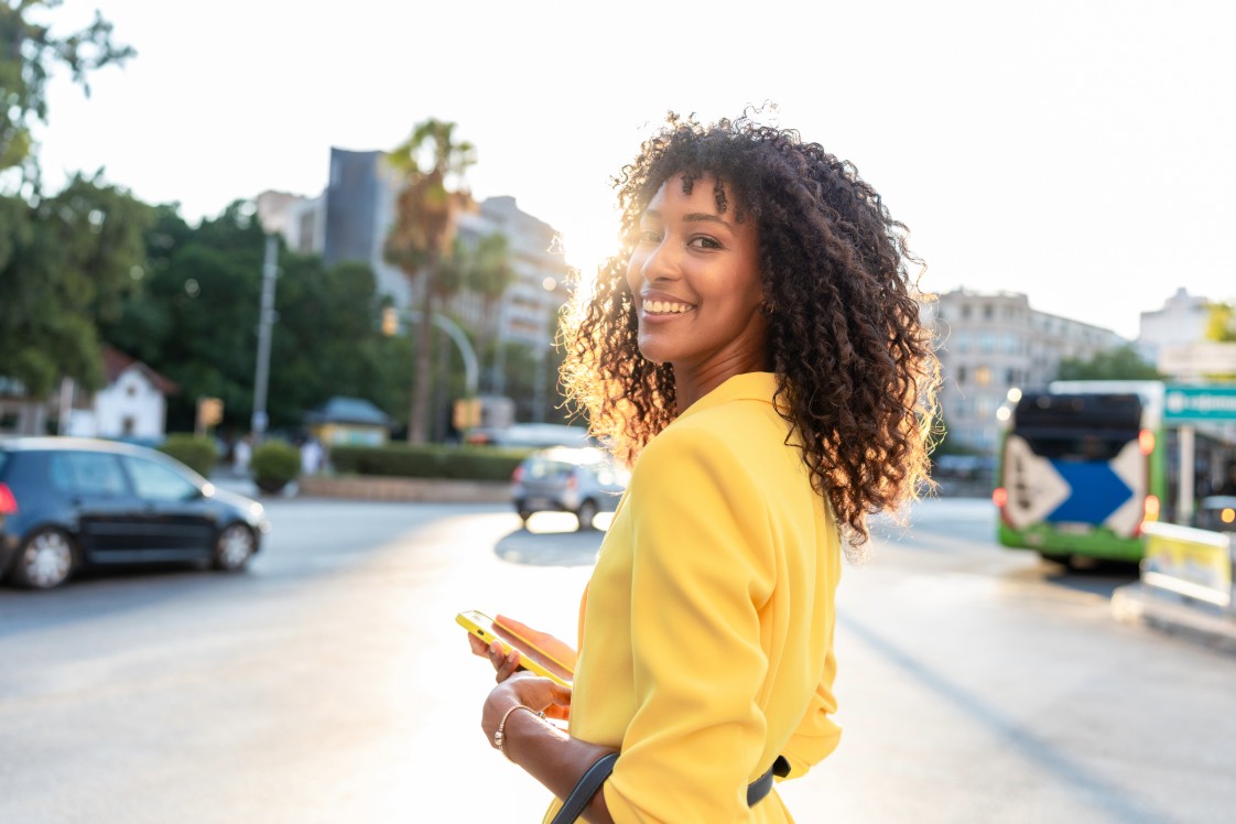 Woman in yellow top, smiling, walking in an urban environment.