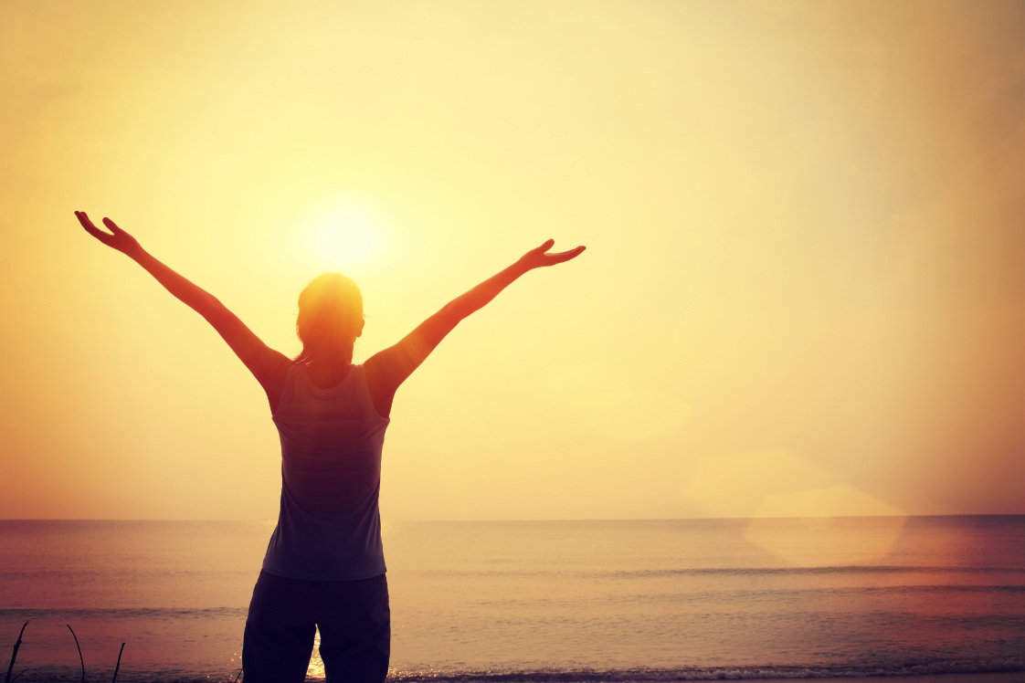 Person outside extending arms with a sunset in the background.