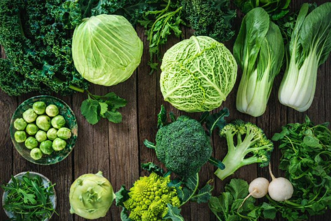 Abundance of green vegetables, including broccoli and kale on a wooden surface.