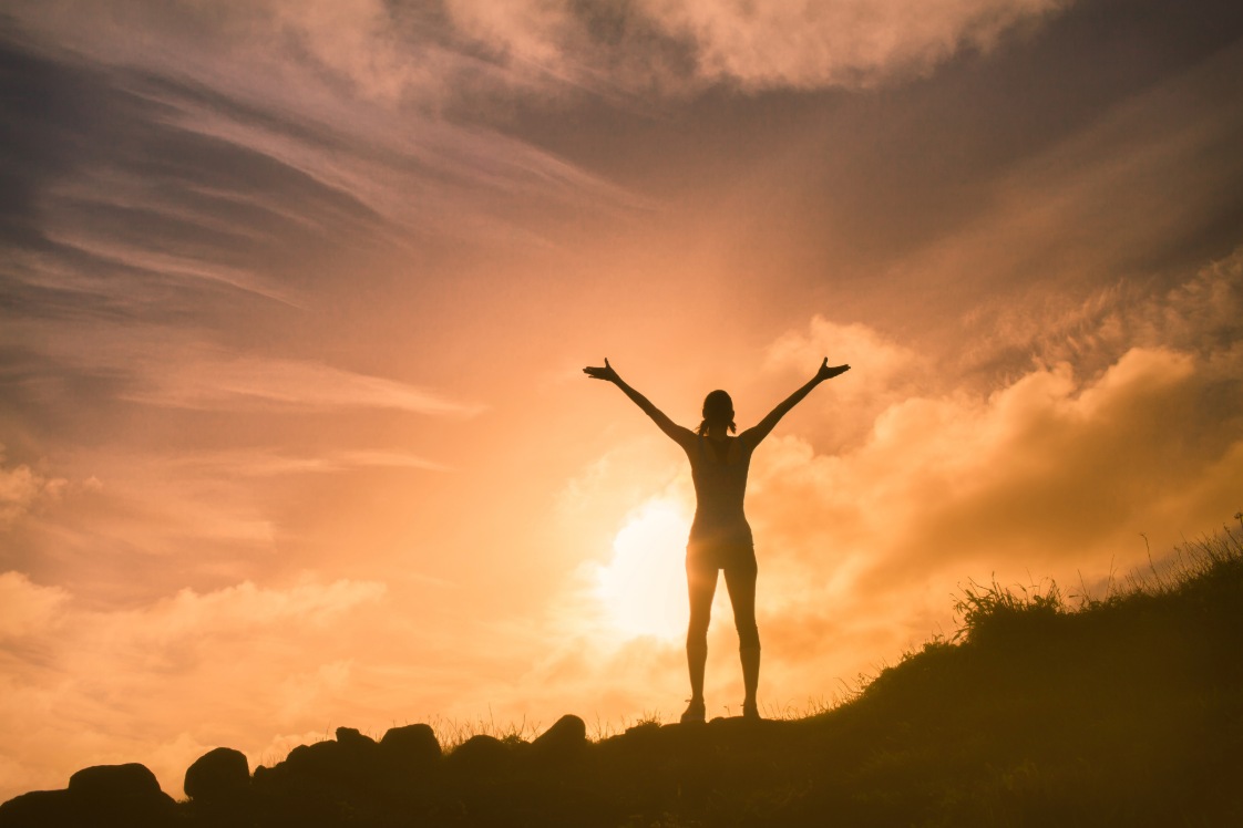 Person outside with arms extended and with a sunset in the background.