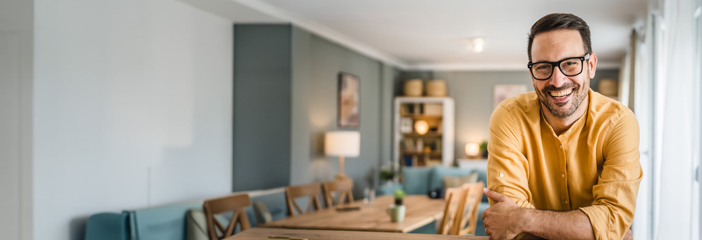 Man in a yellow sweater with arms crossed in a living room setting.